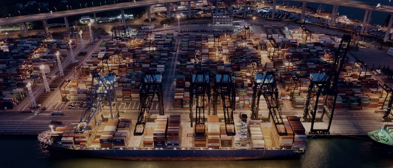 A container terminal at night, stacks lit by yard lighting with a ship alongside.